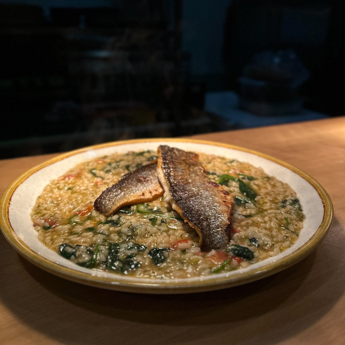 Sea bass and spinach risotto plated under a pendant lamp